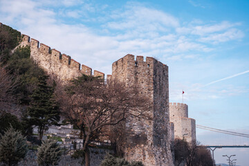 View of Rumeli Fortress. Side view of the 15th century Ottoman Empire castle its many of towers from the street with Fatih Sultan Mehmet Bridge and cemetery.