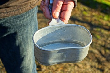 one aluminum empty camping old one with a handle retro cup bowler hat in the hand of a man dressed...