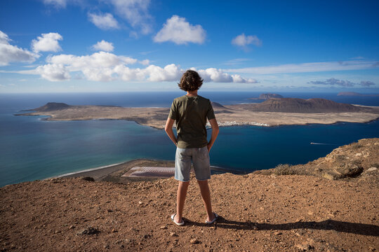 A teenager stands on the edge of a cliff and looks at La Graciosa island from Mirador Del Rio (viewpoint). Lanzarote. Canary Islands. Spain.
