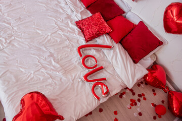 Top view of balloon in form of inscription Love lies on white bed among red pillows. Surprise for...