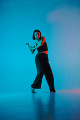 Young woman in black pants and top poses in studio against neon blue background. The dancer...