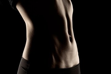 Close-up of a fit woman's stomach under the glow of light in a dark background - obrazy, fototapety, plakaty