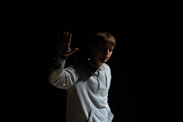 Guy in light street clothes poses on black background of studio. Dancer demonstrates elements of choreography in hip hop style. Modern street dance style.