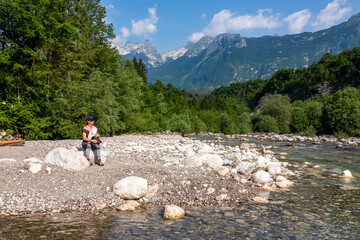 Woman with baby carrier with scenic view of Soca River, Bovec, Triglav National Park,Slovenia. Magnificent Soca Valley in Julian Alps. Wanderlust in untamed Slovenian Alps. Hiking in alpine wilderness - obrazy, fototapety, plakaty