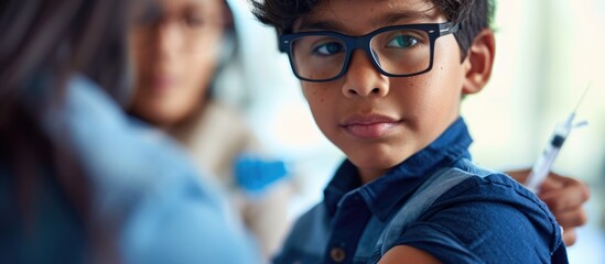A young Latino boy, 6, with glasses and a blue shirt, displays his bandaged arm after receiving a Covid-19 vaccine in the post-Coronavirus era.