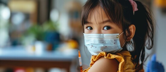 Child immunization concept: Asian girl displays arm post-COVID Delta vaccination. - obrazy, fototapety, plakaty