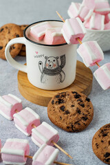 Cup with a fun design with cocoa and white and pink marshmallows and Americano cookies.