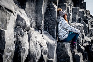 Woman in silver coat and beanie next to basalt formations in Reynisfjara, Iceland