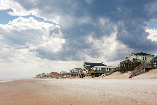 A wide sandy beach and homes with a worker on one roof, clouds dominating the sky over coastal north carolina
