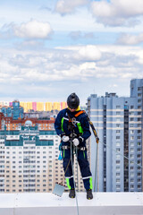 Industry mountaineering worker working on roof building during high-rise work. Rope access laborer in work uniform helmet on rooftop of house. Concept of industrial urban works. Copy ad text space