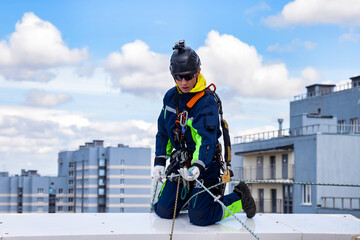 Industrial mountaineering worker in work uniform helmet on roof building during high-rise work. Rope access laborer working on rooftop of house. Concept of industry urban works. Copy ad text space