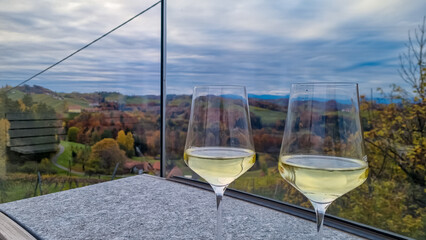 Obraz premium Drinking a glass of white wine with scenic view of vineyard during summer in Maribor wine region, Slovenia, Europe. Luxury couple get away vacation. Enjoying beverage in serene and romantic ambiance.