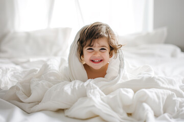 Obraz na płótnie Canvas Smiling kid wrapped in a white blanket on a bed