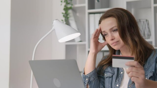 Upset woman in front of laptop with credit card in hand Lack of funds on the account. Negative balance on card. Cancellation bank or refusal credit limit. Sad woman because high prices, too expensive