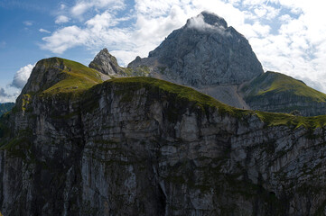 Top peak of mount Mangart  (2679 m) with north west wall falling towards Italy. On the ridge is a path leading towards mountain peak surrounded with some bright clouds.
