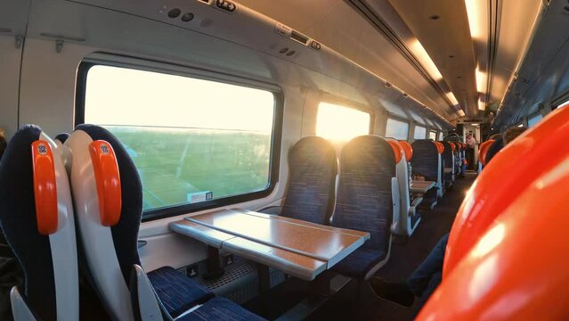 Sunrays peek through window above empty passenger seats on the intercity train. Comfortable seating on a modern express train that travels through the Scottish countryside in golden morning light.