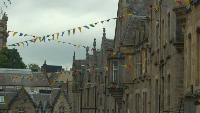 Fluttering colorful flags hanging between beautiful old medieval townhouses. Picturesque stone facades of historical buildings decorated with bunting flags. Festive mood in old part of historic city.