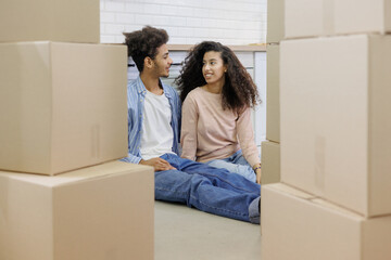 happy young African American couple is moving new home. man and woman are sitting among cardboard...