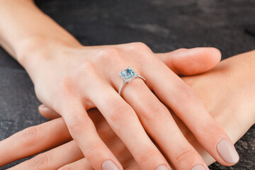 Beautiful female hand with gold ring with diamonds and aquamarine on gray background
