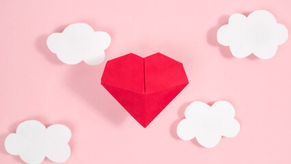 Red voluminous origami heart above white clouds. Symbol of love. Concept of valentine's day holiday, wedding and other occasions. Flat lay.