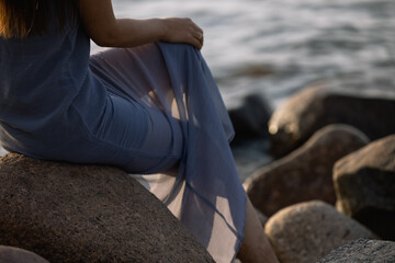 Beach vacation, woman swinging her naked legs sitting on stone pier on sea background. Skin covered by water drops, concept of foot care, tanning and summer holiday