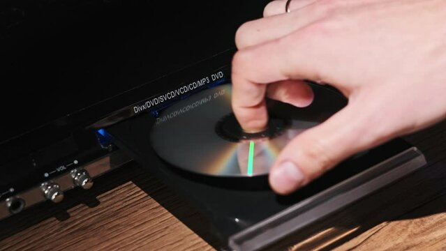 DVD compact disc is inserted into the player. Male hand loads CD into a CD player tray close-up. Music, movies, or data recorded on a laser optical information storage medium. Loading Compact Disc