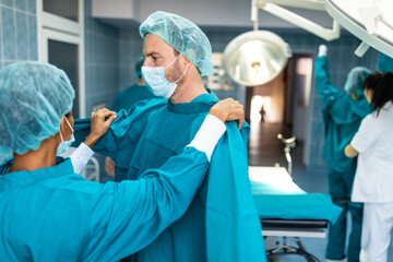 Two surgeons helping each other get dressed in preparation for a surgery with colleagues. Team of...