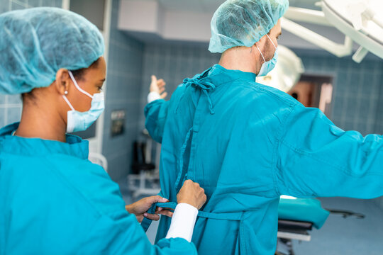 Female surgeon tying surgical gown for male colleague in operating room. Two surgeons helping each other get dressed in preparation for surgery in operating theatre.