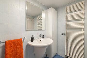 Mirror, sink and towel dryer in modern tiled bathroom