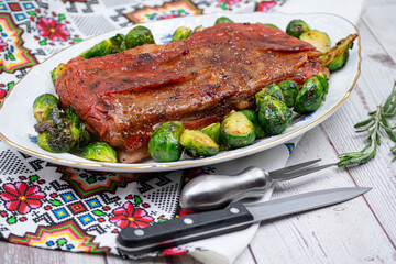 Vegan pork belly roast made with seitan and starch, served on oval plate along with roasted Brussels sprouts. Wooden table, stylish setting