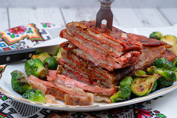 Vegan pork belly roast made with seitan and starch, served on oval plate along with roasted Brussels sprouts. Wooden table, stylish setting
