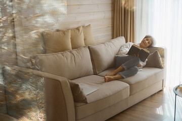 Smiling elderly woman relaxing with a book on cozy sofa