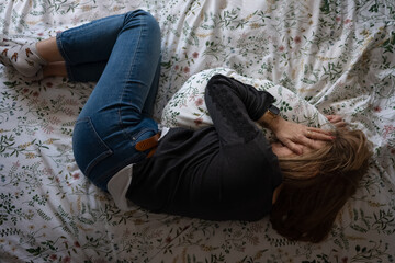 Woman curled up in bed while suffering from mental health issues and depression.