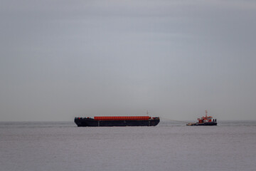 Orange tug boat towing a barge out to sea