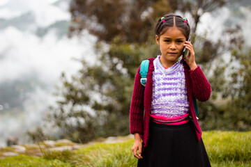 Una niña campesina con mochila conectada con celular en la mano, estilo de vida rural, Niña bonita comunicándose con celular , niña  inteligente se comunica con entusiasmo en conferencia en línea con 