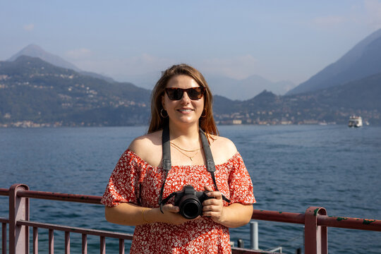 Happy brunette 30s woman enjoying summer holidays. Concept of vacation and travelling. Varenna, Italy. Lake Como. Redhead girl holding a camera outdoors at summer day