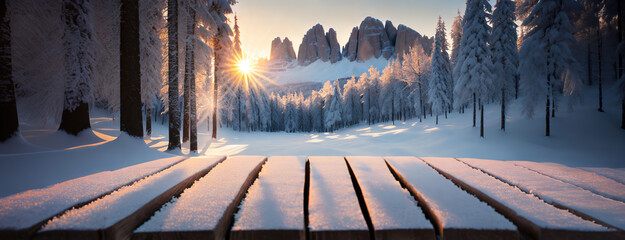 The sun sets behind rocky mountains, casting a golden glow over the snow-covered Dolomites and illuminating a wooden bench in the foreground. Panorama with copy space.