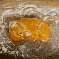 Barra de pan sobre una mesa de madera llena de harina.  - obrazy, fototapety, plakaty