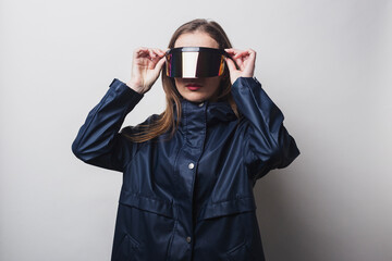 Young woman wears virtual reality glasses, in a blue jacket on a light background