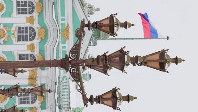 the Russian flag on the building of the Winter Palace through vintage lamppost is waving in the wind in a snowfall, the crown of the Russian Empire on a bas-relief