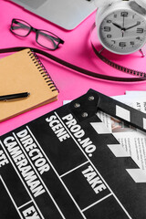 Notebook with movie clapper, film reel and alarm clock on pink background