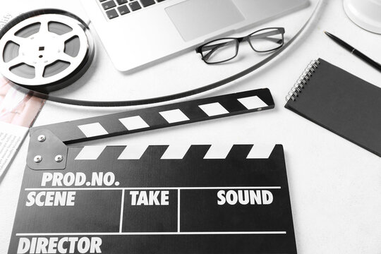 Movie clapper with film reel, eyeglasses and laptop on white background