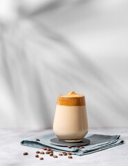 Dalgona coffee. Whipped instant coffee in a glass with beans and shadow on a light background.