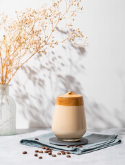 Dalgona coffee. Whipped instant coffee in a glass with beans and shadow on a light background