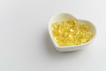 yellow fish oil capsules in a heart shaped plate on a white background