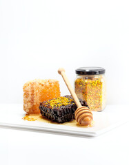 Two sorts of the bee honeycomb with jar of bee pollen and honey dipper isolated on white background. Different types of honey combs close up view. Brown and golden honeycombs with wooden honey stick.