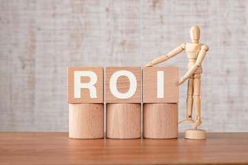 There is wood cube with the word ROI. It is an abbreviation for Return On Investment as...
