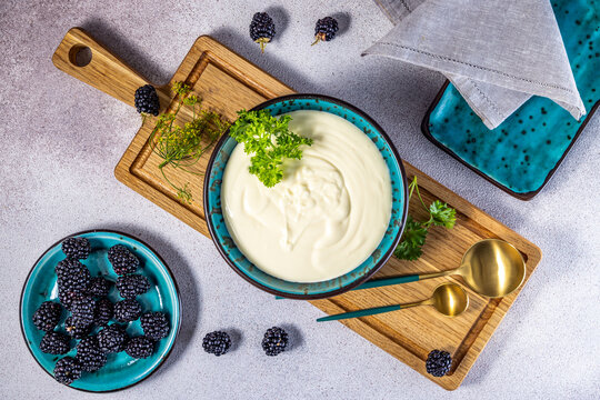 Sour cream in bowl surrounded by many fresh berries and herbs