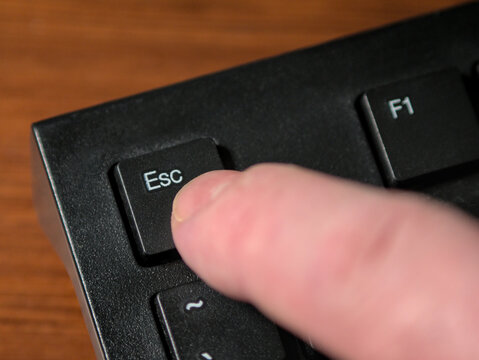 A person's finger pressing the Escape key on a black computer keyboard. Close up, macro shot