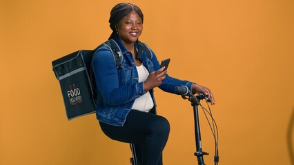 Healthy black woman balancing technology and customer service, effortlessly cycling through city to...